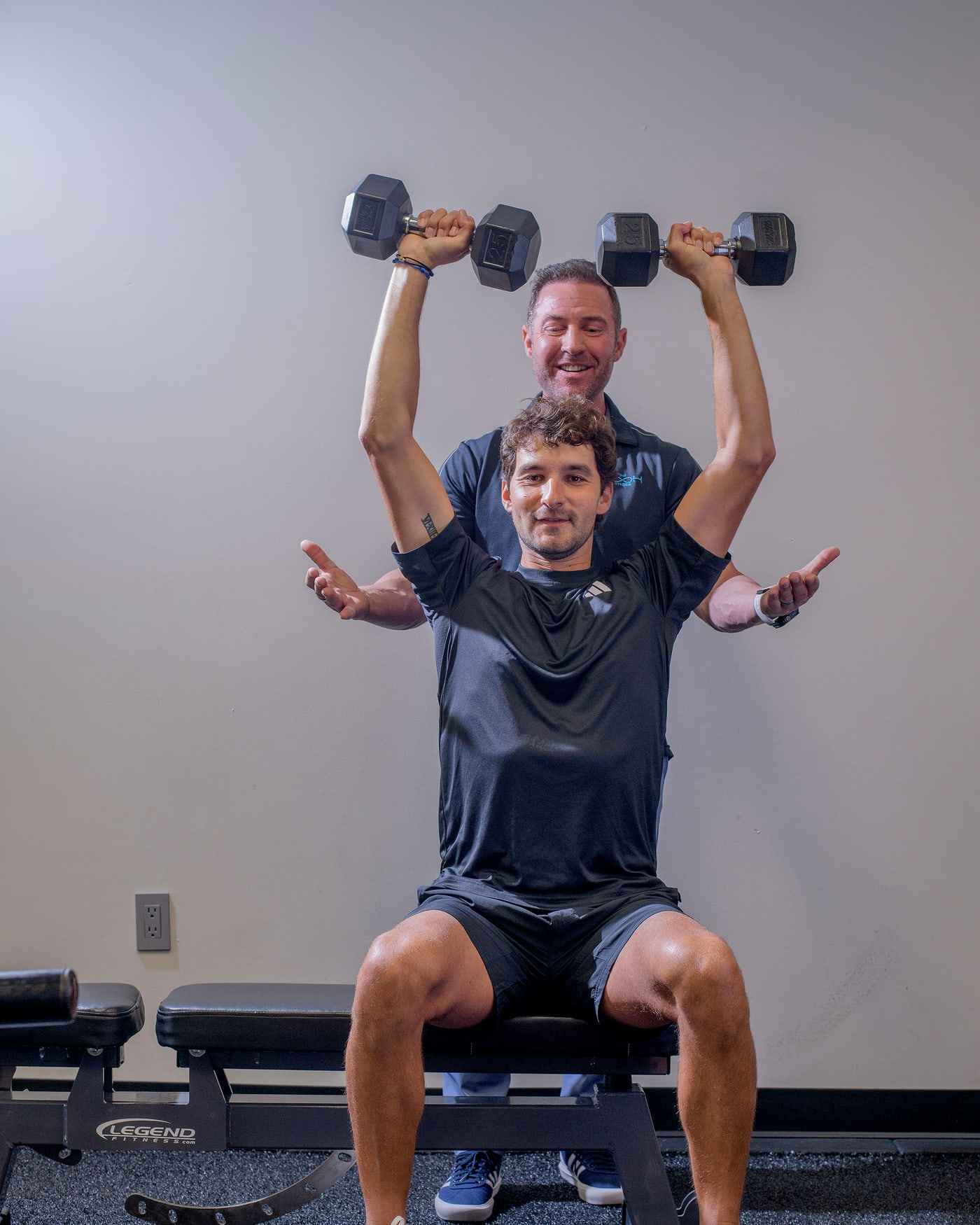 Bryan Greene spotting a client’s dumbbell overhead press