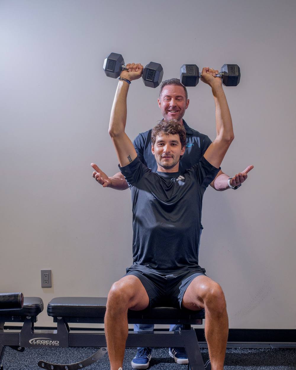 Bryan Greene spotting a client's dumbbell overhead press